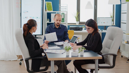 Colleagues doing teamwork on chart presentation for project in boardroom. Workmates using technology and documents for business meeting about marketing strategy and development.