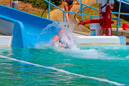 A Woman On A Waterslide Splashes At The End Of Her Slide Down A Water Chute With A Large Wave