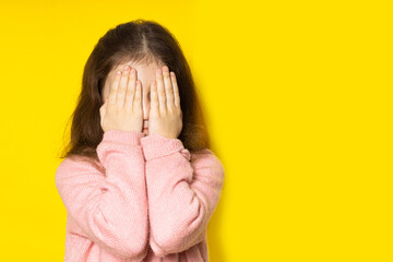 Scared girl. Fearful little girl covered her face with her hands on a yellow background.
