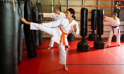 Women and man in kimono exercising with punching bags in gym during karate training.