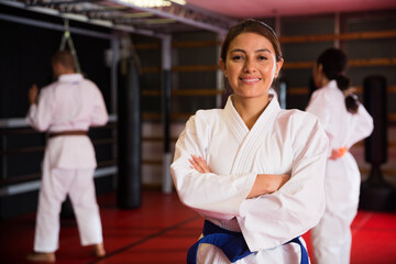 Smiling young Latina in kimono standing with crossed arms in gym