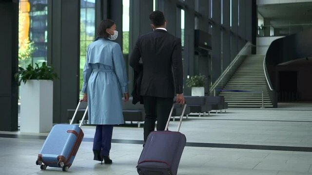 Young business people talking and walking at airport with suitcases in hands spbd. Back view of beautiful businesswoman, businessman have dialogue and walk confidently, move luggage and head to check