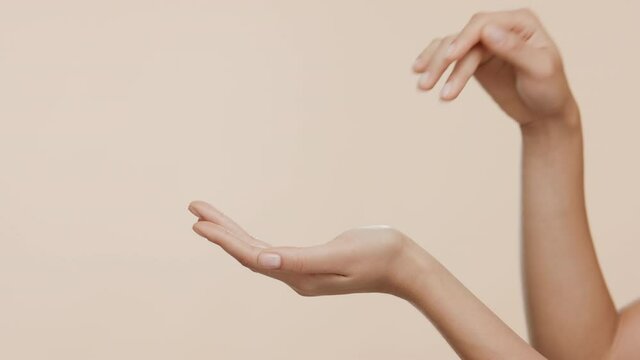Horizontal close-up shot of female skin care model strokes her middle finger and palm on beige background | Cracked hands removal concept