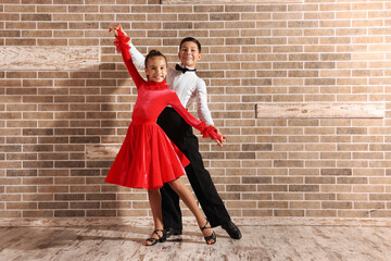 Beautifully dressed couple of kids dancing together near brick wall indoors