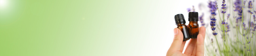 Lavender essential oil banner. Bottles of essential oil in a woman's hand and lavender flowers on a white green, purple background. Cosmetics with lavender extract banner. 