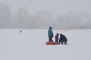 Father, mother and child on winter fishing on frozen lake in winter stormy weather