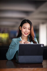 Portrait of Smiling a beautiful young Asian businesswoman sitting with laptop and computer while doing some paperwork at the out office. 