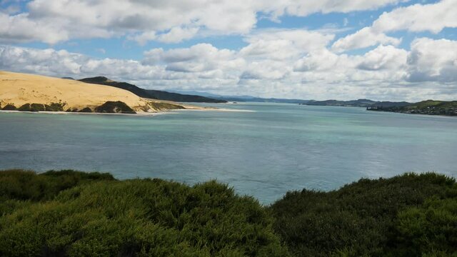 Dolly forward shot of beautiful Kauri Coastline with bush, clear ocean water and sandy mountains during cloudy day 
