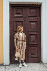 Fototapeta premium Young millennial woman with wild hair dressed in an autumn coat posing near the door of an old building.