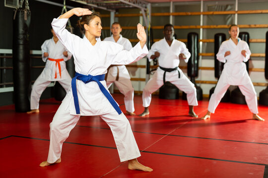 Hispanic woman in kimono standing in fight stance during group karate training.