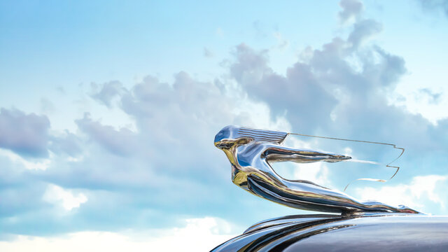 Locomotive 1940s Chevrolet hood ornament  seen from below with sky and clouds in the background.