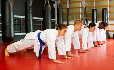 Multiracial group of men and women warming up before karate training and doing push-ups in gym.