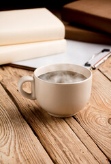 cup of coffee, tea or chocolate, soft beige color with hot steam and notebook on rustic wooden table.