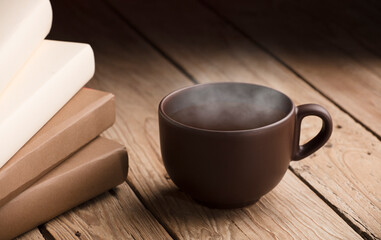 brown cup with chocolate, tea or coffee, hot steam, books on rustic wooden table 