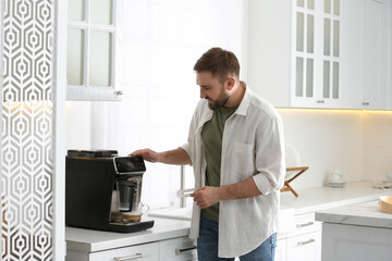 Young man preparing fresh aromatic coffee with modern machine in kitchen