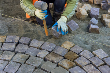 Close-up of construction worker installing and laying stones on road sidewalk