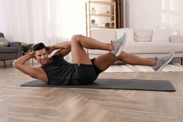 Handsome man doing abs exercise on yoga mat at home
