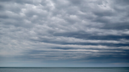 The space of the sky is closed to the horizon by rows of clouds. Moody weather on the seaside.