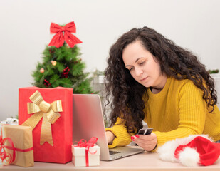 Happy woman holding credit card and shopping online on laptop against Christmas tree in the background. Xmas online shopping, preparing for the New Year, buying present, winter holiday sales concept