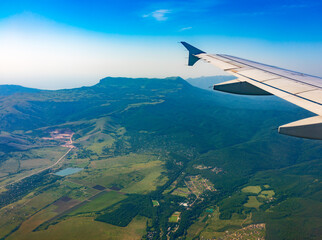 View of airplane wing, blue skies and green land during landing. Airplane window view.