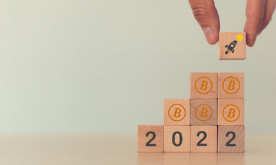 Cryptocurrencies growth concept in 2022. Bitcoin to the moon. Blockchain technology, digital currency market. Hand puts the wooden cubes with BTC growth icon to 2022 on warm background and copy space.