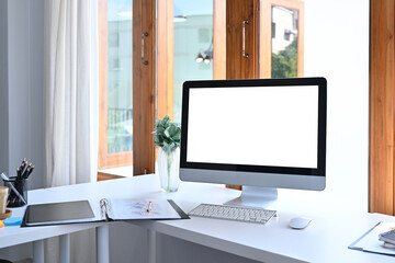 Modern workspace with computer, office supplies and houseplant on white table.