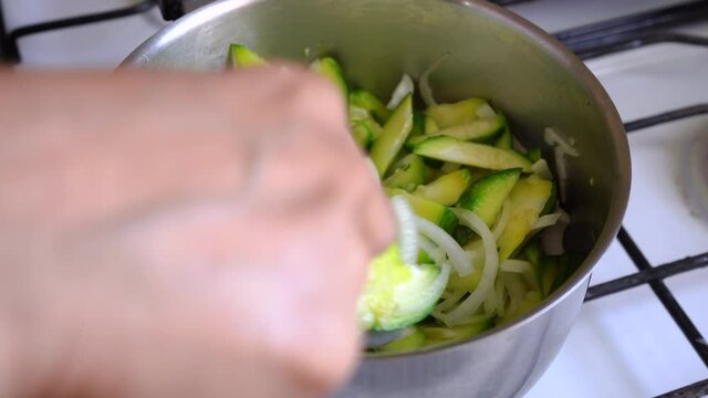 Cooking Fresh Green Squash With White Onions In A Pot, Stirring With A Spoon. close up