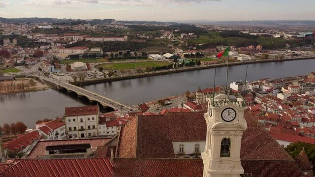 Aerial zoom in University's clock tower in coimbra cityscape drone view of the river and the bridge with Portugal flag