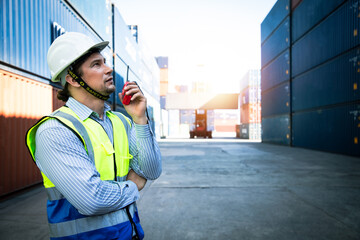 Obraz premium Portrait of handsome engineering using walkie talkie for control labor in front of container store. Back view of forklift transport on background of cargo store. Export and transportation 