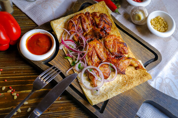 On a dark countertop, a light linen napkin, on a cutting board Fried four quails in pita bread with red onion rings, on a linen napkin, cutlery, red pepper, rosemary branch.