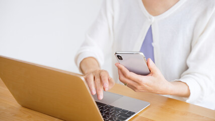スマホを見ながらパソコンに入力するシニア女性