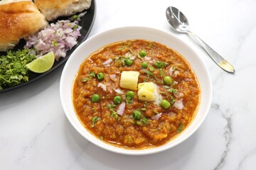 Indian Mumbai Street style Pav Bhaji, garnished with peas, raw onions, coriander, and Butter. Spicy thick curry made of out mixed vegetables served with pav over white background with copy space.