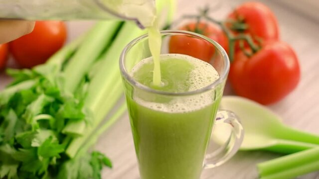 Healthy Vegan Green celery Smoothie. celery juice with sprig of tomatoes on background. celery juice is poured into a glass. slow motion