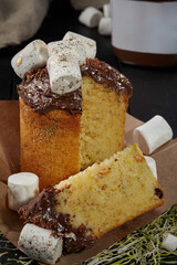 Sliced Easter cake of fluffy dough with candied fruit topped with chocolate icing and marshmallows
