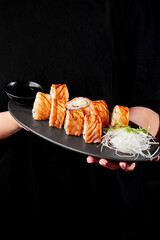 Female hands holding plate with sushi rolls with seared salmon