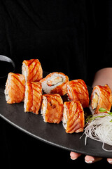 Waitress hands holding plate with sushi roll with seared salmon, cream cheese, red tobiko and apple