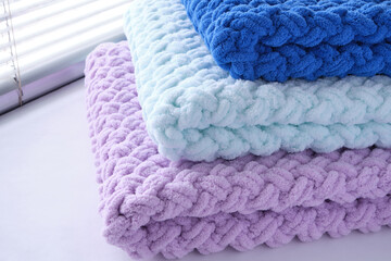 Warm, delicate and plush handmade baby blankets in three colors of blue, lilac and mint on background of window.