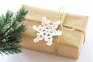 Christmas and New Years background close-up. Gift box wrapped in kraft paper with jute cord. Decorated with a crocheted snowflake and a branch