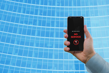A man's hand holds a smartphone with the notification 'No service' against the background of a business building with a blue glass facade. Notification 'No service' on the smartphone screen