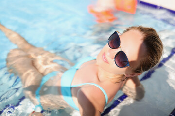 Happy young female sit in pool wearing trendy glasses