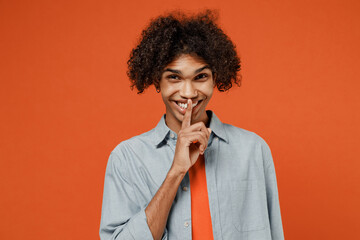 Young secret fun student black man 50s wearing blue shirt t-shirt say hush be quiet with finger on lips shhh gesture isolated on plain orange color background studio portrait People lifestyle concept