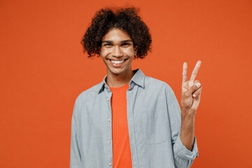 Young smiling happy cheerful fun student black man 50s wearing blue shirt t-shirt look camera showing victory sign isolated on plain orange color background studio portrait. People lifestyle concept.