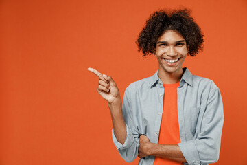 Young black man 50s wearing blue shirt t-shirt point index finger aside on workspace area mock up copy space area isolated on plain orange color background studio portrait. People lifestyle concept.