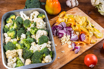Cauliflower and broccoli cut into pieces in a baking tray on the kitchen table with cut vegetables...