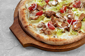 Delicious pizza Caesar style with white sauce, chicken, parmesan, egg, cherry tomatoes and fresh lettuce at wooden background. Restaurant pizzeria menu with delicious taste pizza Caesar.