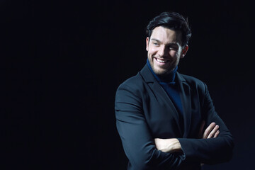 Portrait of Smiling Handsome Caucasian Brunet Businessman Wearing Black Suit Posing With Folded Hands Looking Aside Against Black