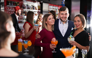 Young man and two women with cocktails having fun at nightclub