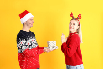 Cute couple in Christmas clothes on yellow background