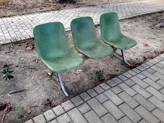 Old faded green plastic chairs in the park. Connected together for people to rest