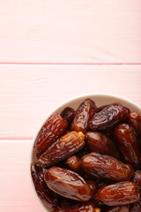 Bowl of dried dates on pink wooden background.